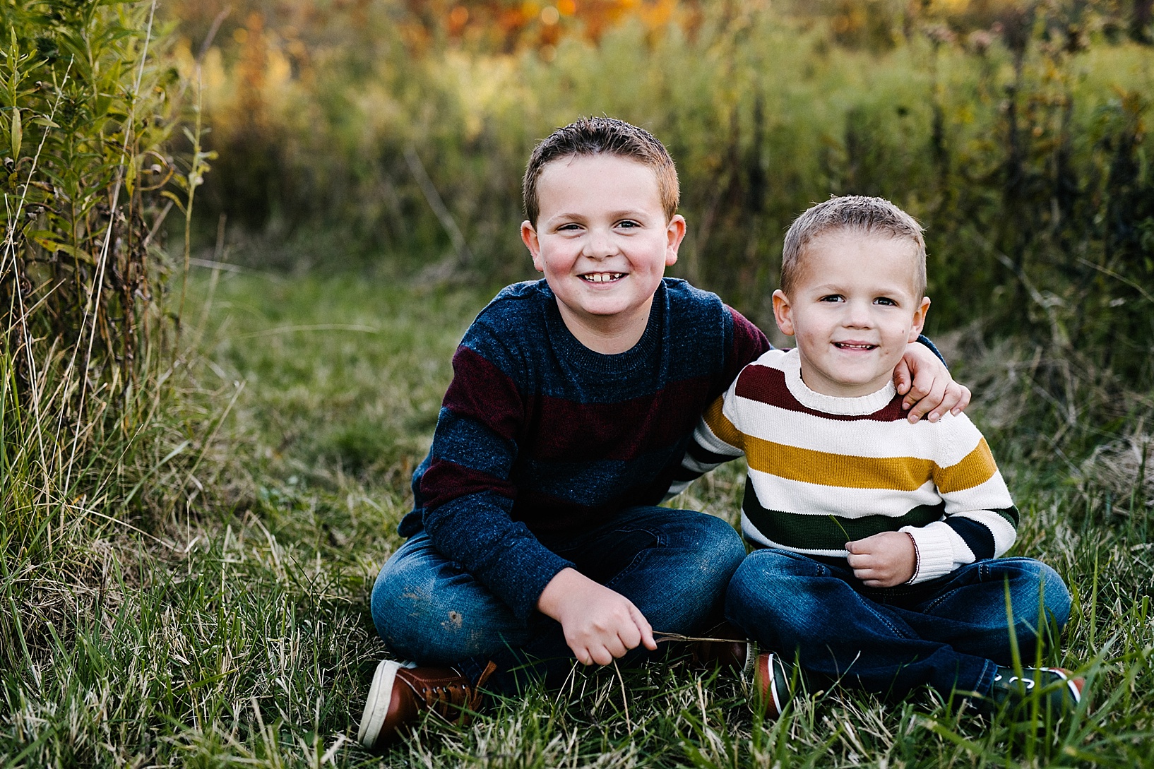 young boys wearing fall sweaters sitting in field