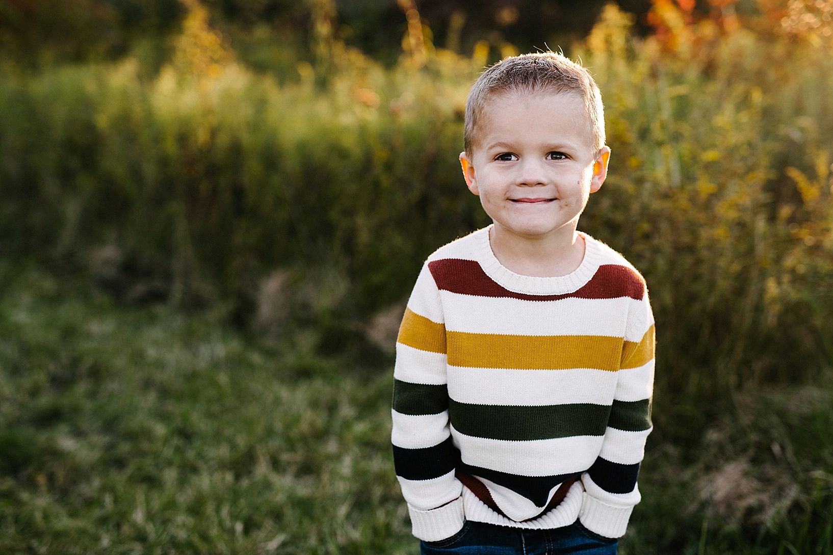little boy in striped sweater standing in field smiling