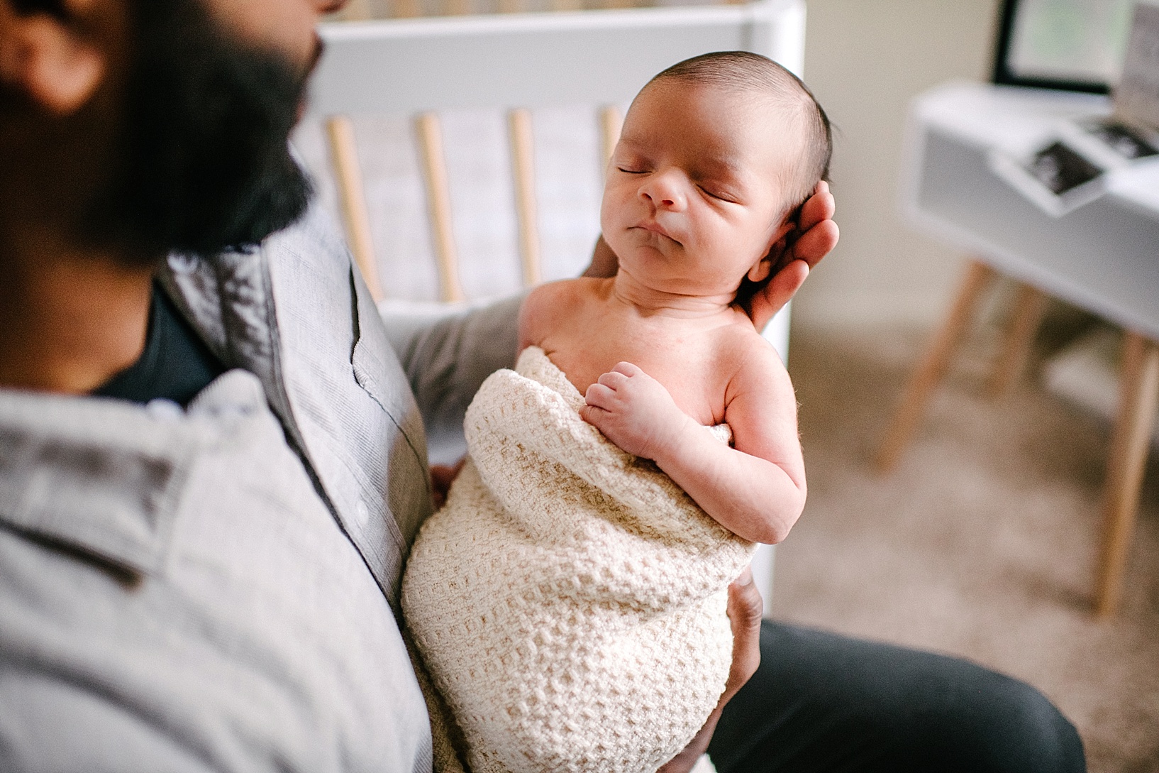 father holding newborn baby wrapped in blanket in nursery