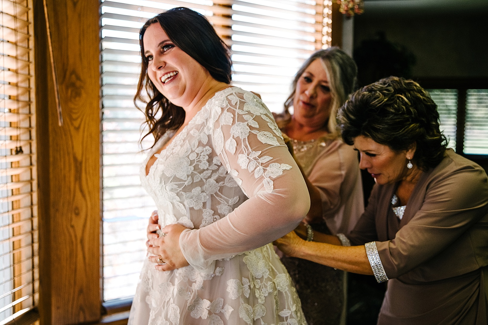 bride's mothers helping her into wedding dress