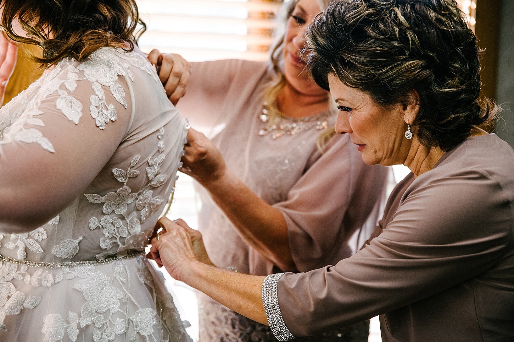 mother of the bride buttoning bride's dress