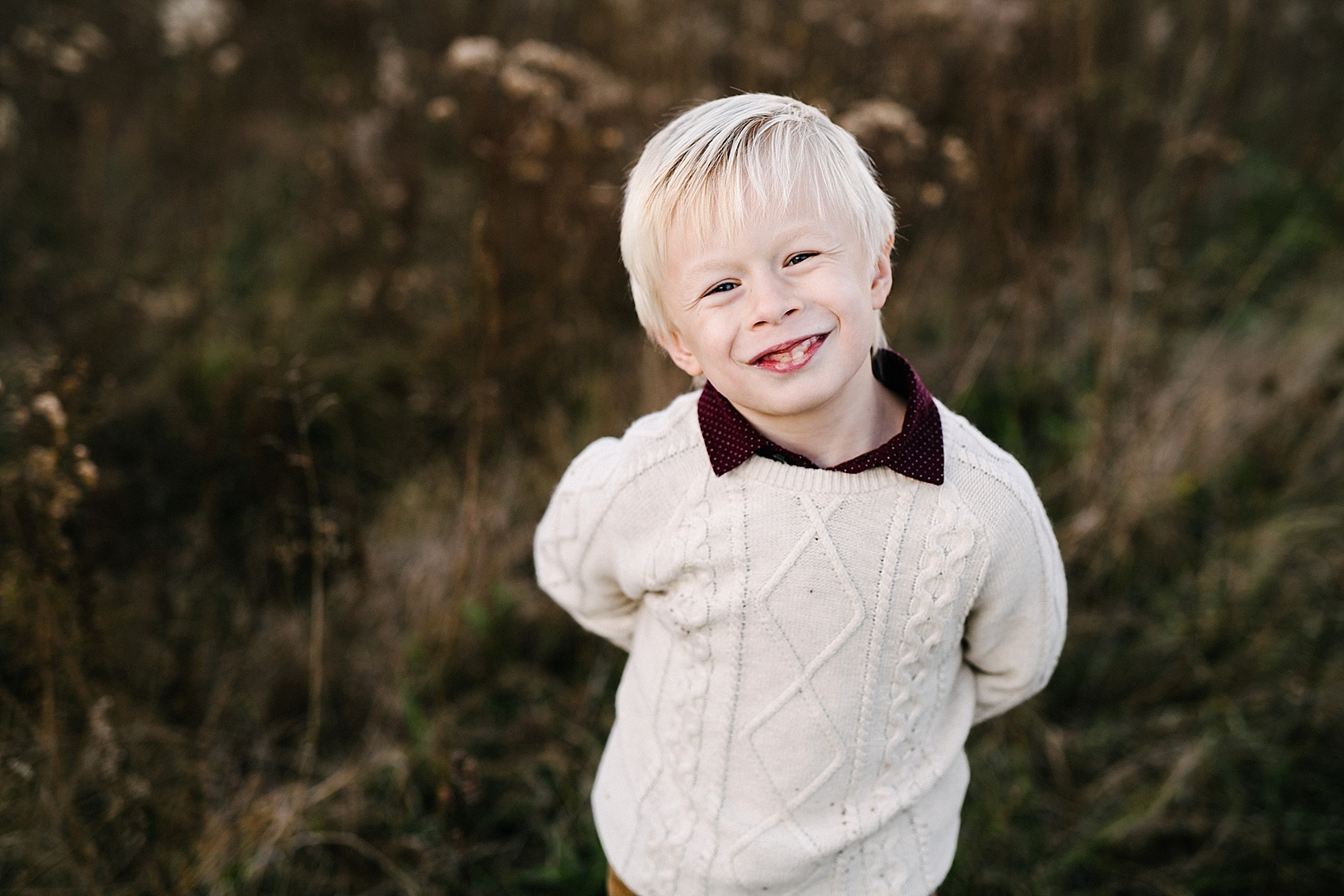 little boy wearing cable knit sweater standing in field