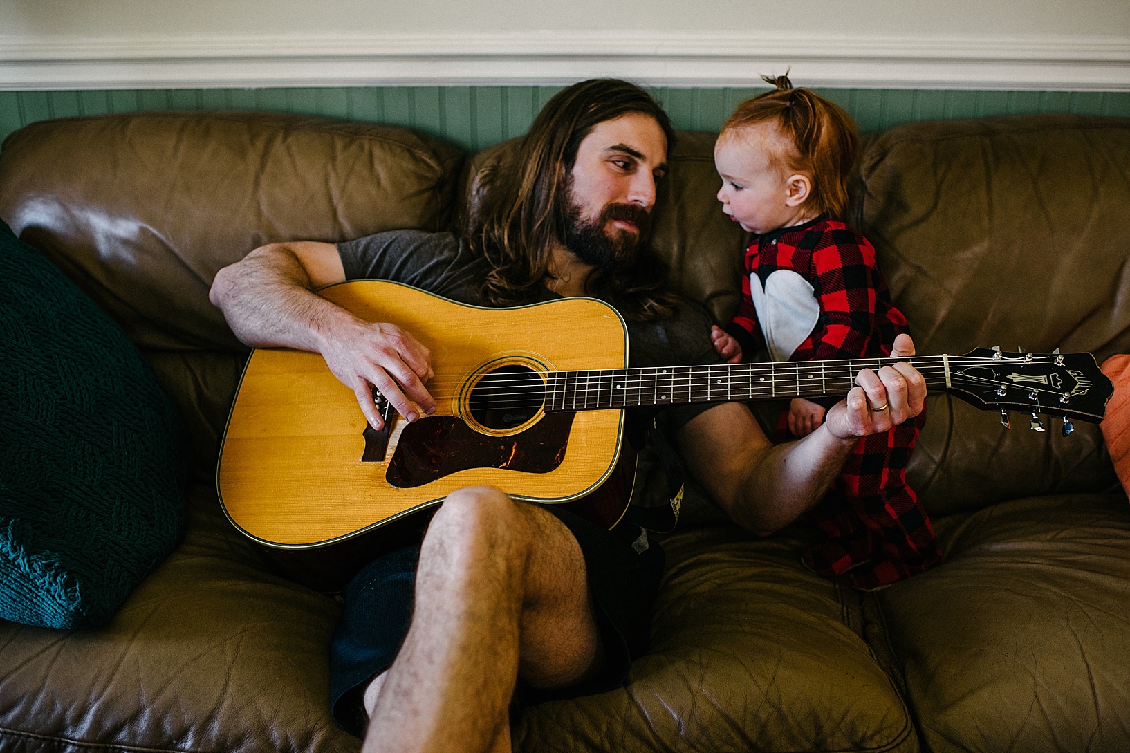 dad playing guitar on couch with toddler daughter