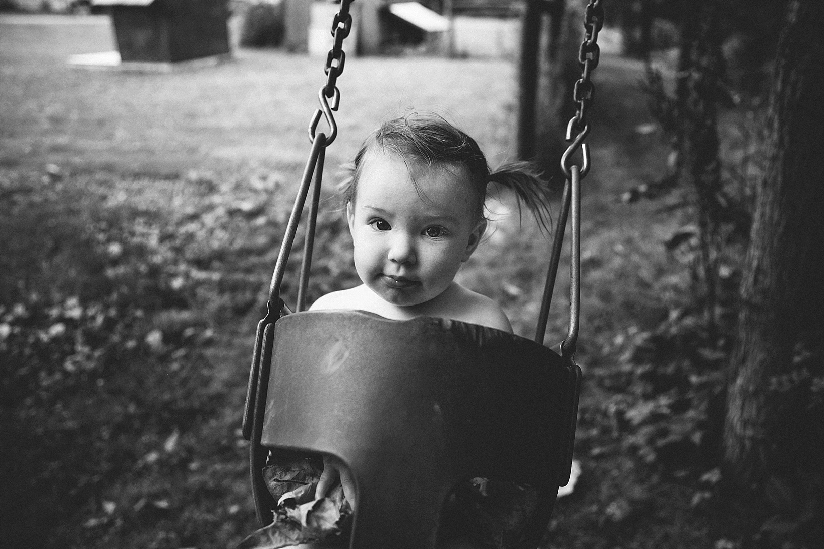 little girl with pigtails swinging in backyard swing