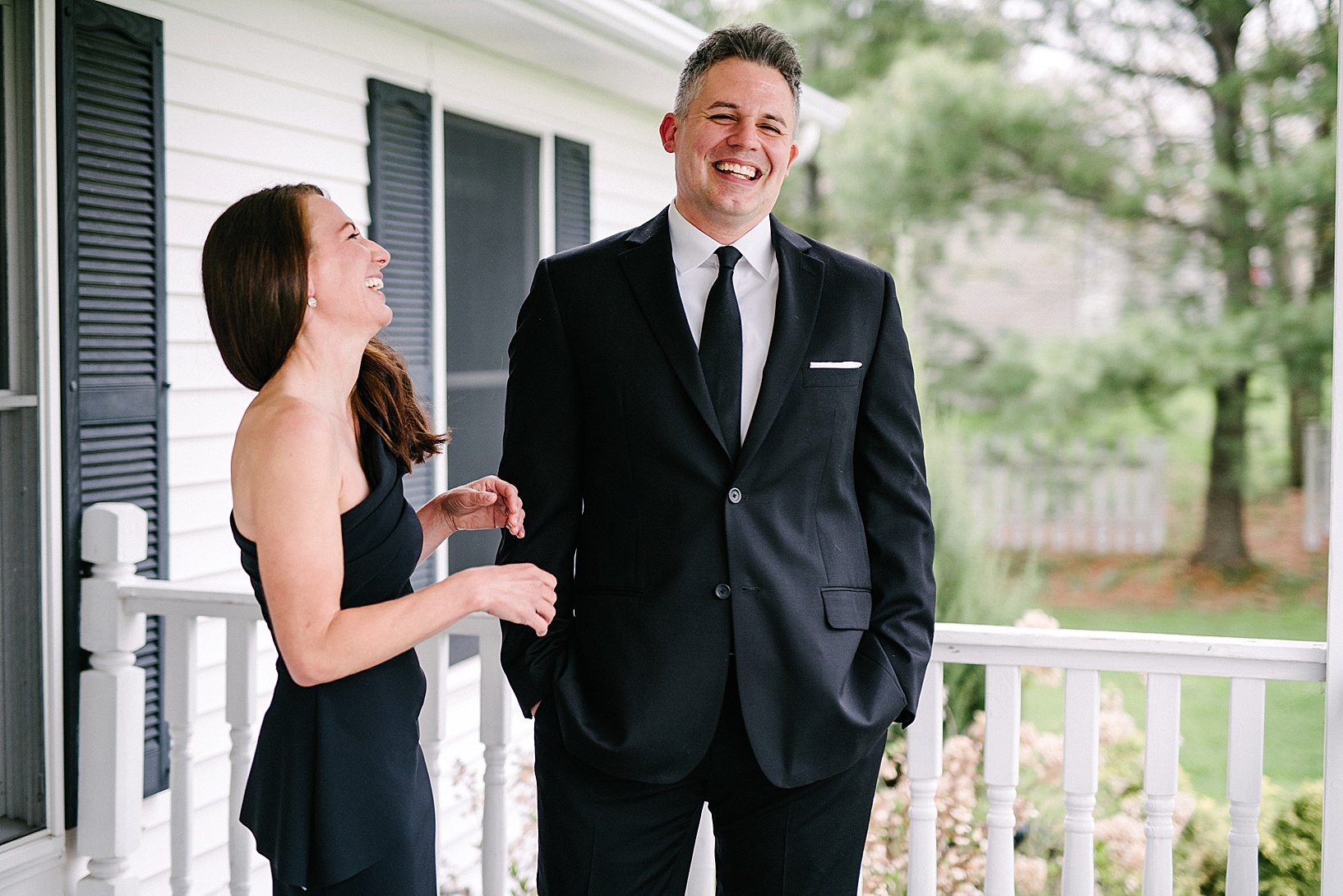 couple in formal attire laughing on front porch during engagement session