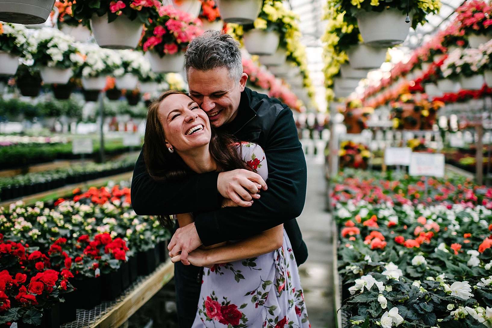 man hugging woman wearing floral dress in a greenhouse