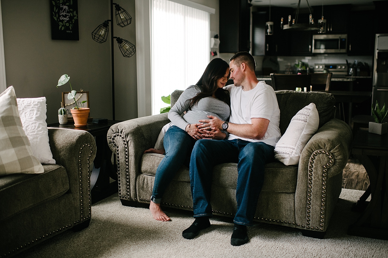 Husband and pregnant wife hug on couch with neutral nursery maternity photography shoot