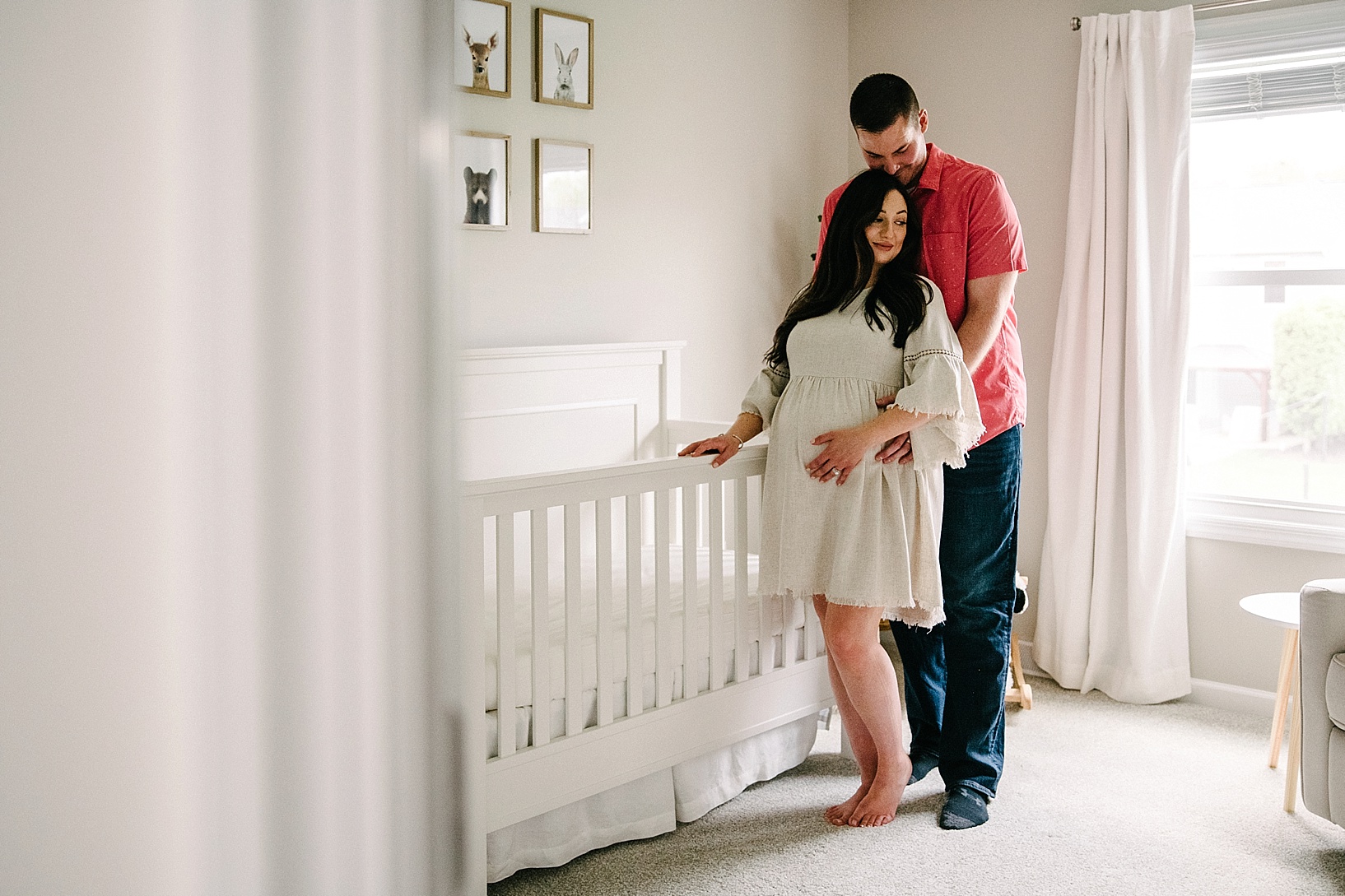 Husband holds pregnant wife in neutral nursery