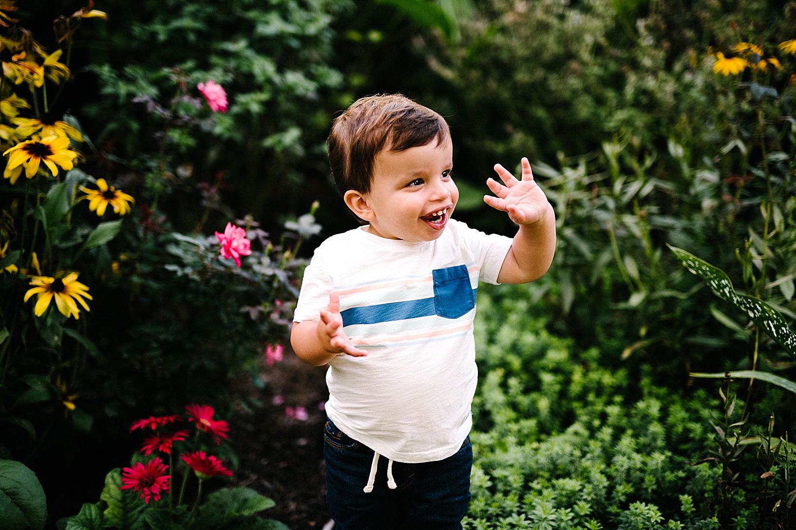 Young boy smiles and waves while surrounded by gorgeous flowers at Western Village Reserve