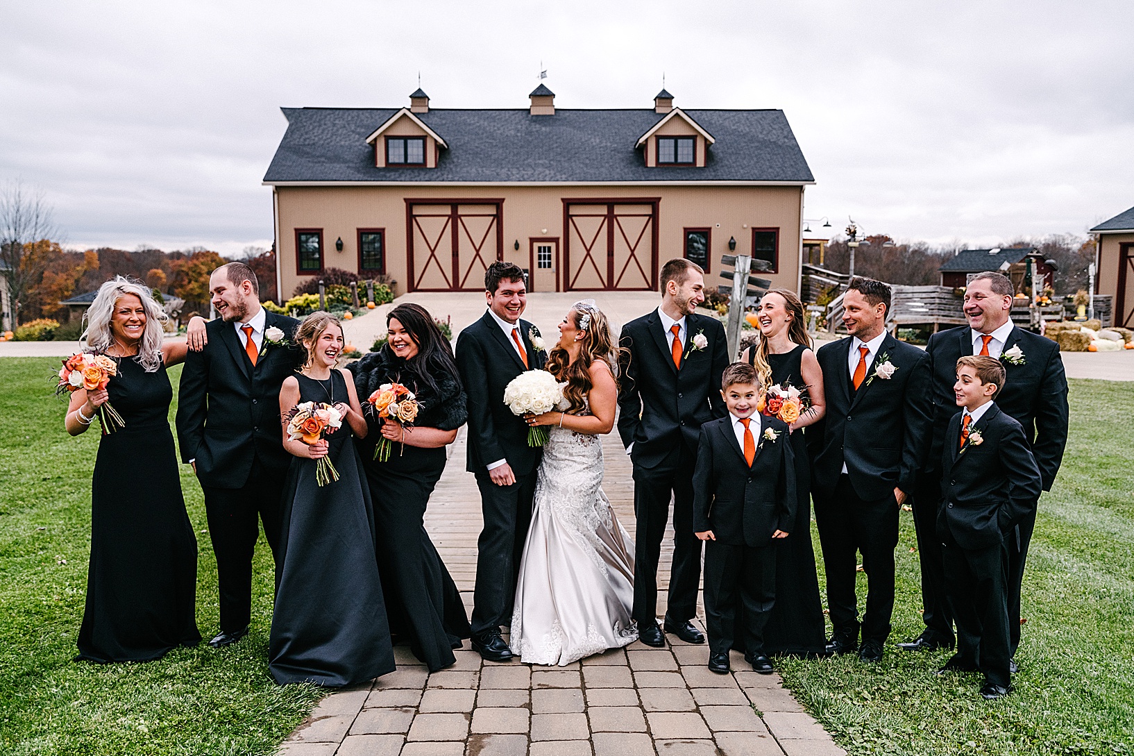 Bridal party stands in front of the barn at Peacock Ridge and smiles and laughs.