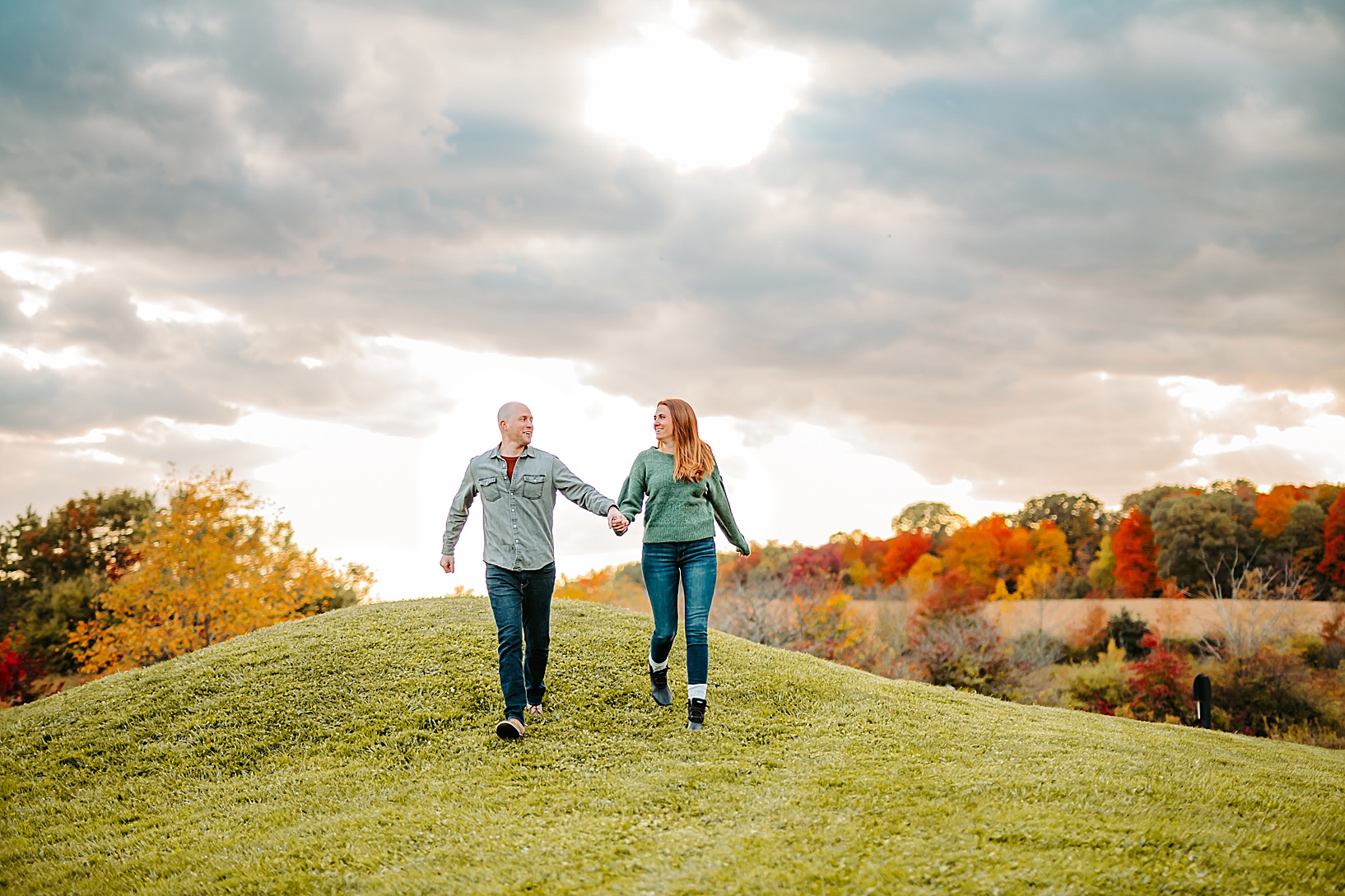 man and woman holding hands and running down hill laughing