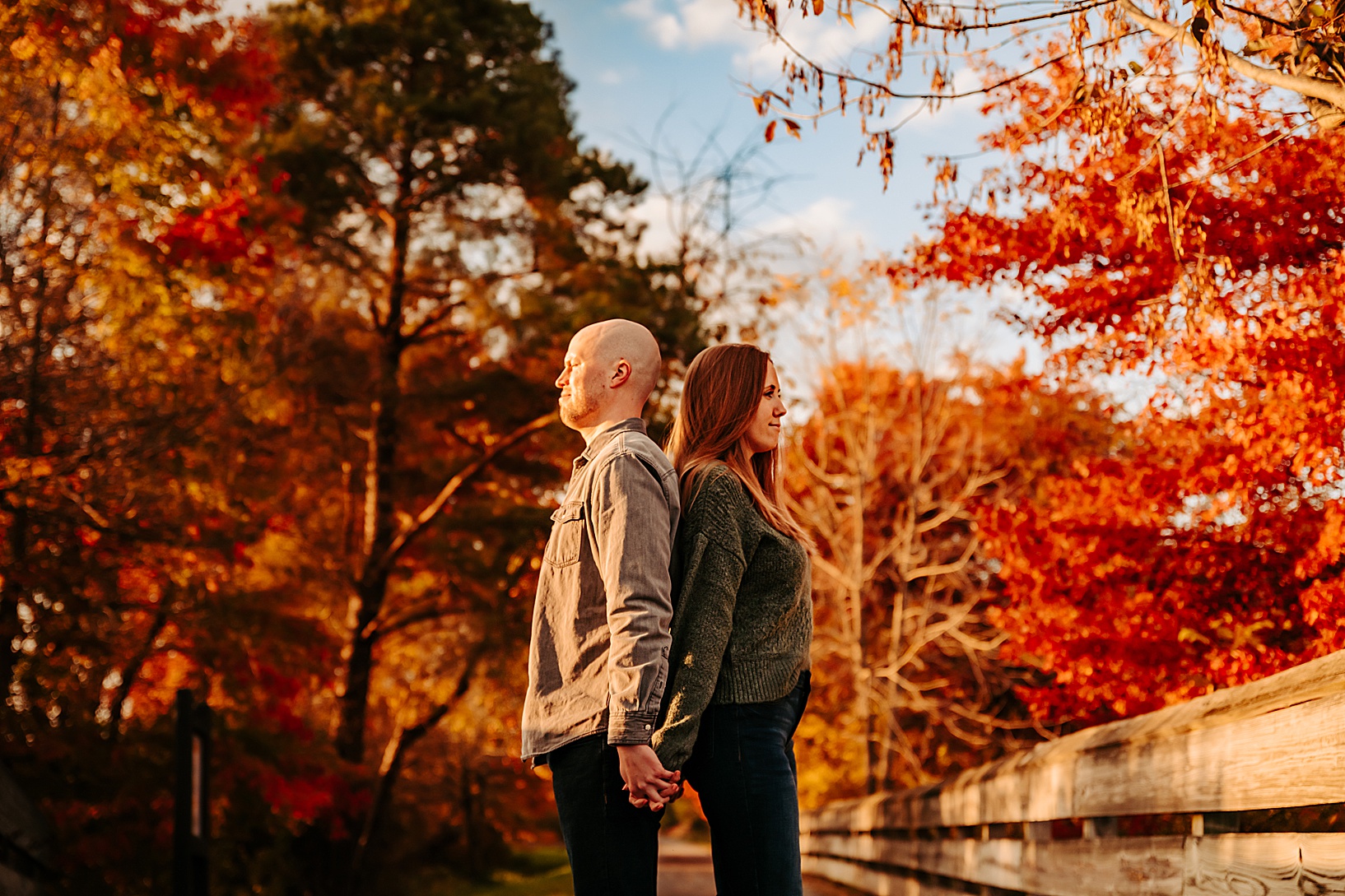 man and woman standing back to back with autumn trees in the background