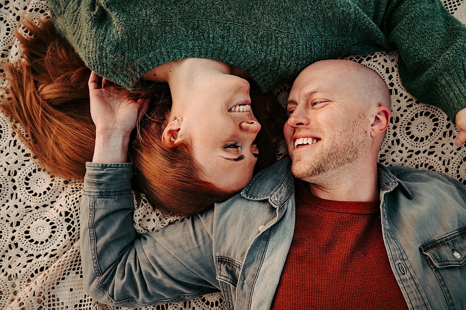 man and woman laying on lace blanket smiling at each other