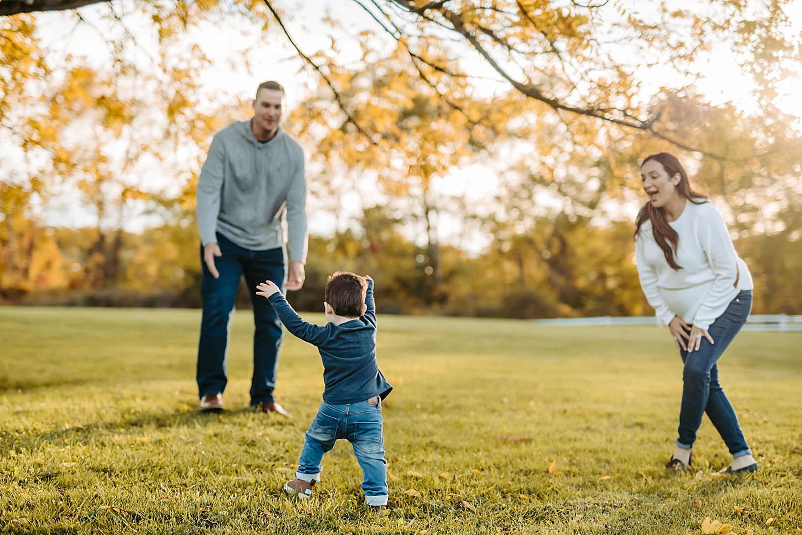 toddler boy walking towards dad with outstretched arms as mom looks on