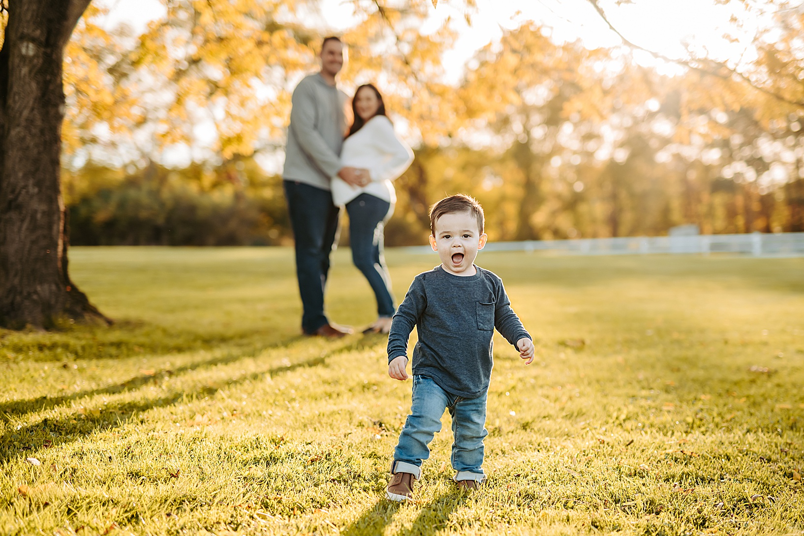 young boy walking and smiling while pregnant mother and father stand in the background