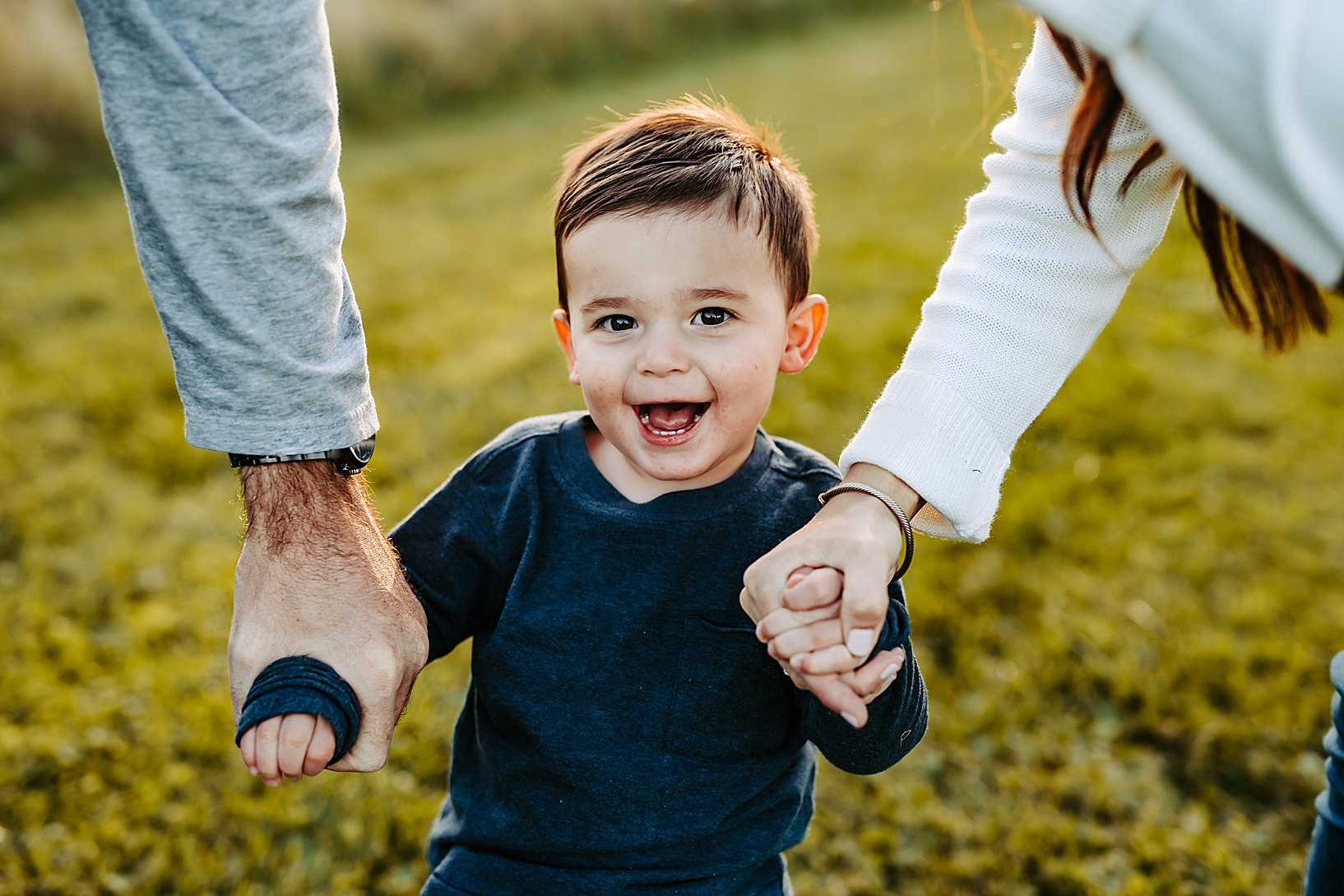 young toddler holding hands with parents and smiling