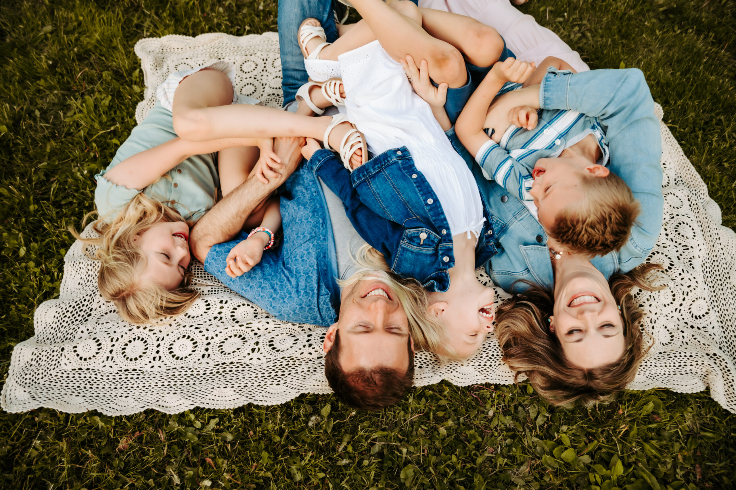 family with three kids laying on blanket in grass laughing