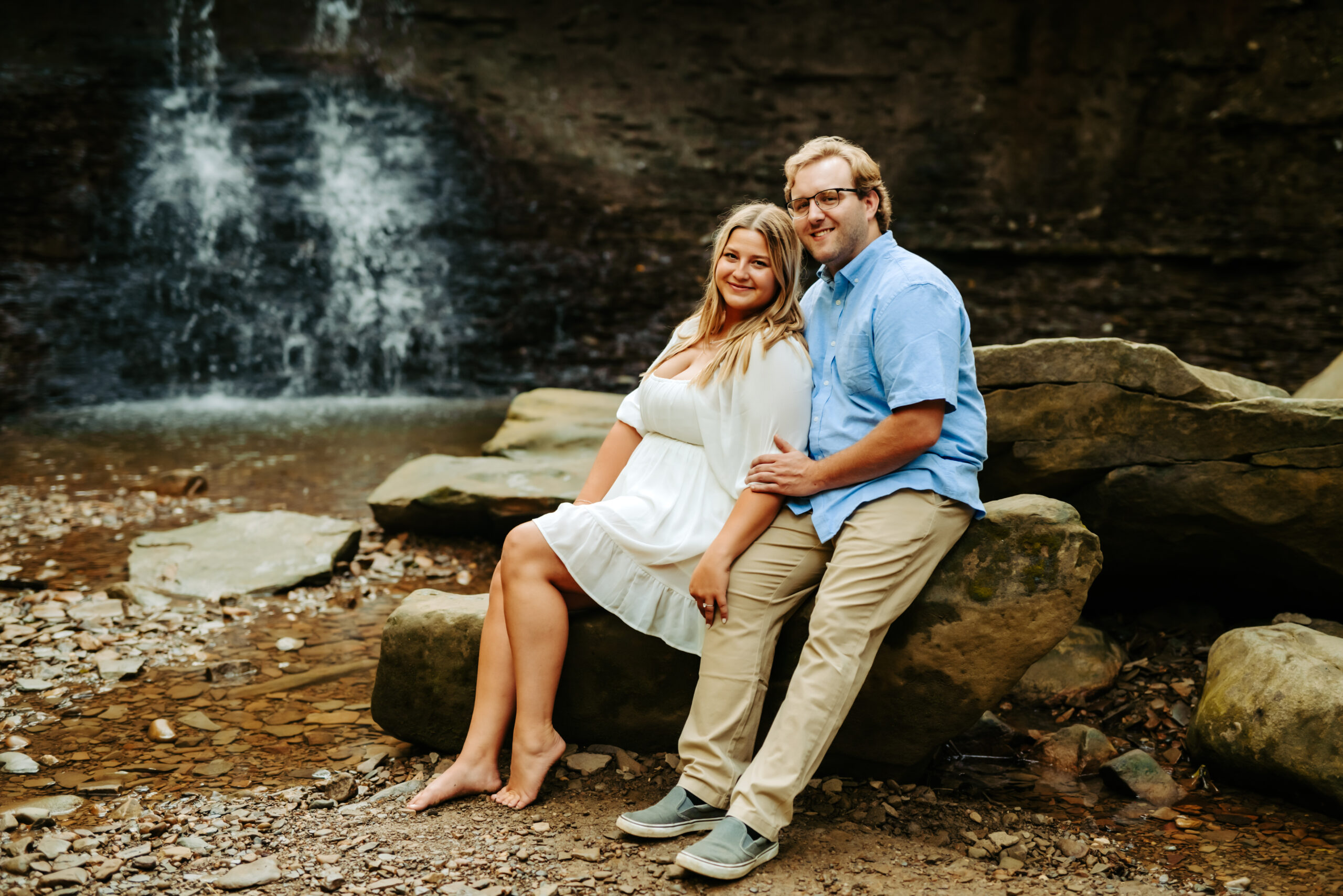 engaged couple sitting on rock in front of blue hen falls in cuyahoga valley national park