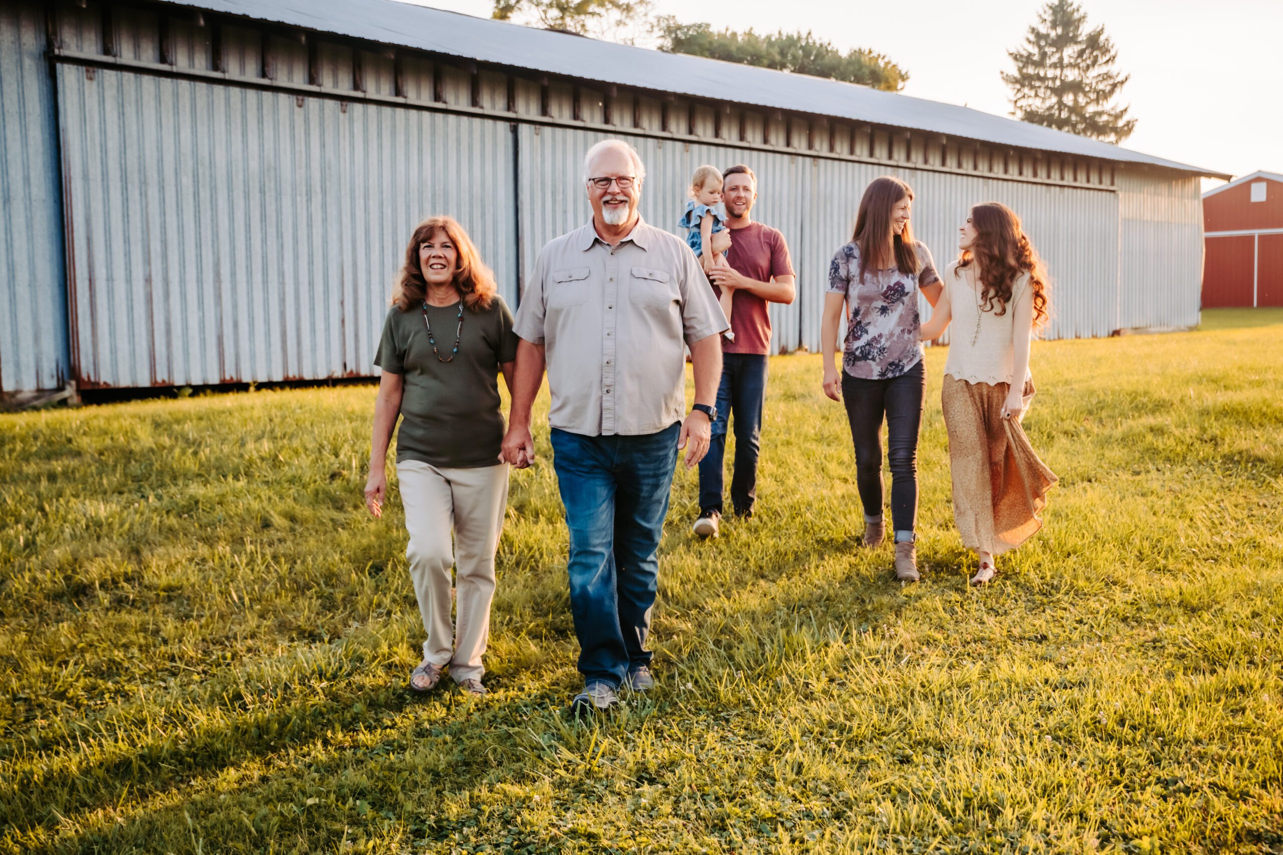 family walking across field in front of barn laughing together