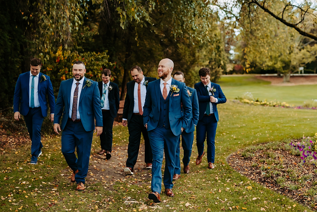 groom wearing navy blue suit walking across Fellows Riverside Gardens with groomsmen