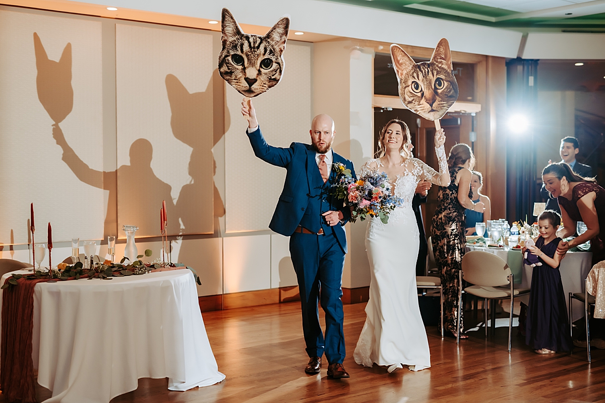 bride and groom entering wedding reception carrying cat cardboard cutouts