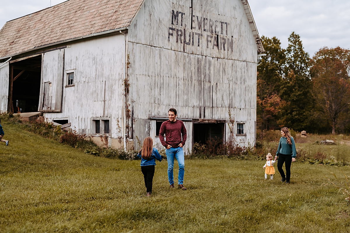 man and woman walking with young kids in front of old white barn