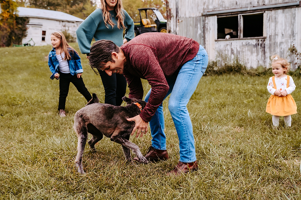 man playing with his dog while wife and kids look on in the background