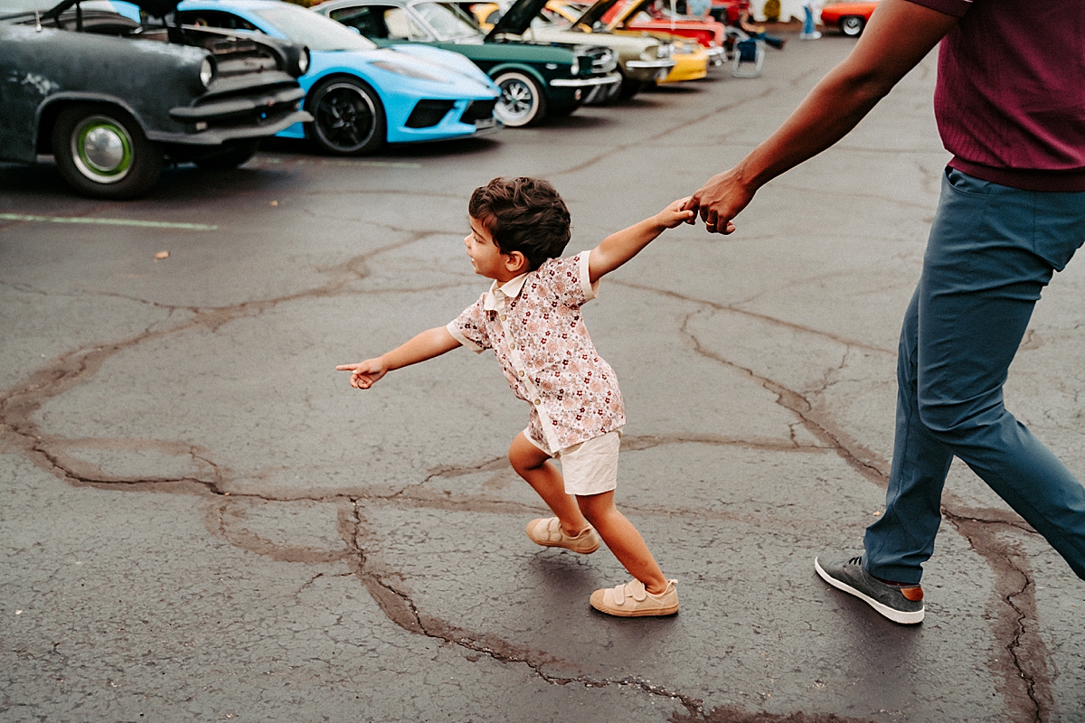 little boy holding dad's hand pulling him across parking lot to look at old cars