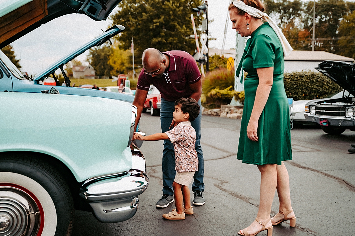 parents with young boy looking under hood of car at car show