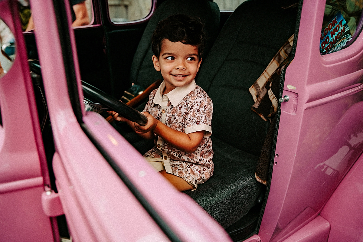 young boy sitting in driver's seat of purple car pretending to drive