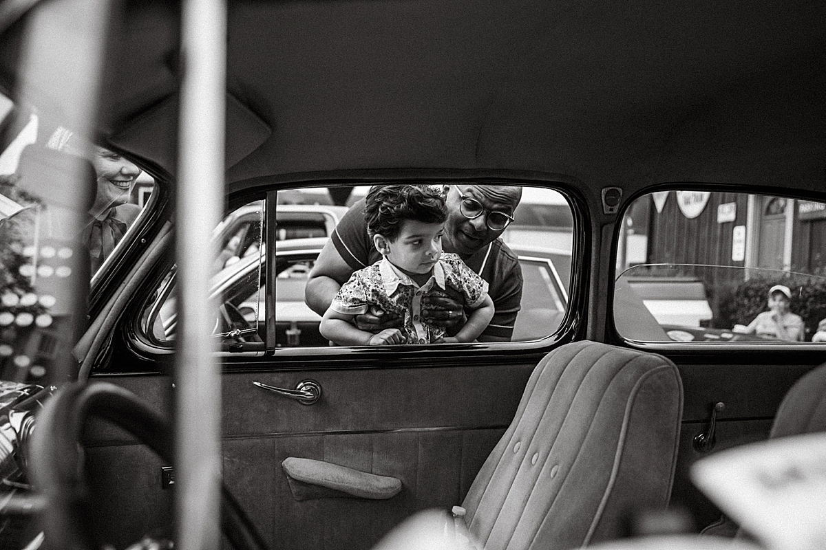 dad holding young son up to peek into backseat of a car at a car show