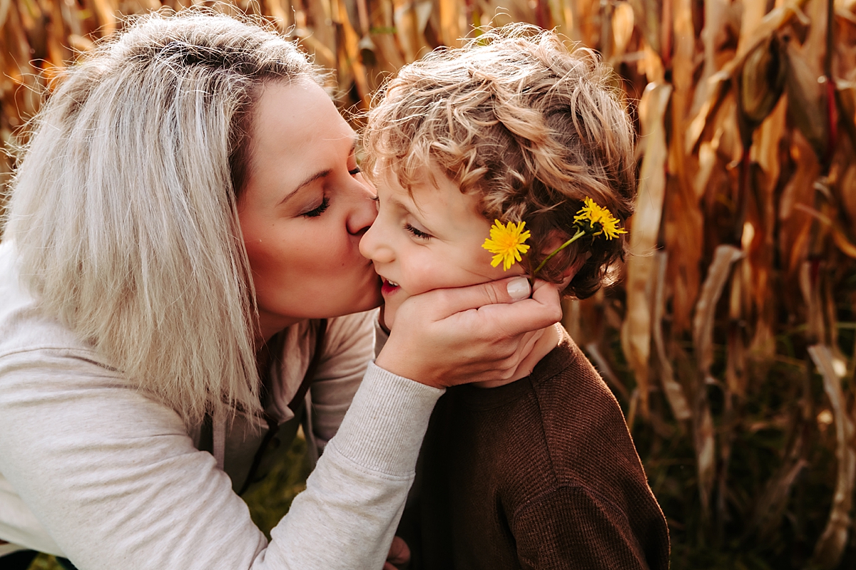 mom holding dandelions and kissing son's cheek