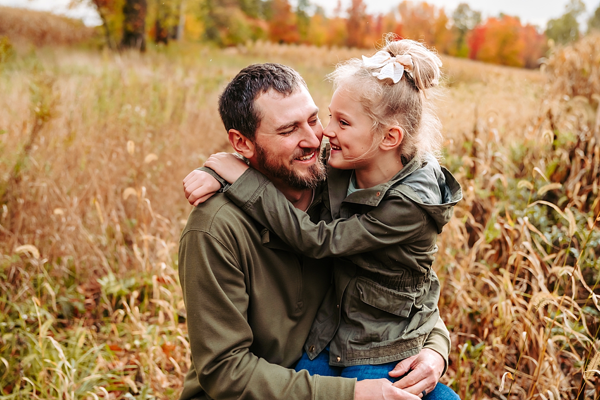 dad holding daughter on his lap in field