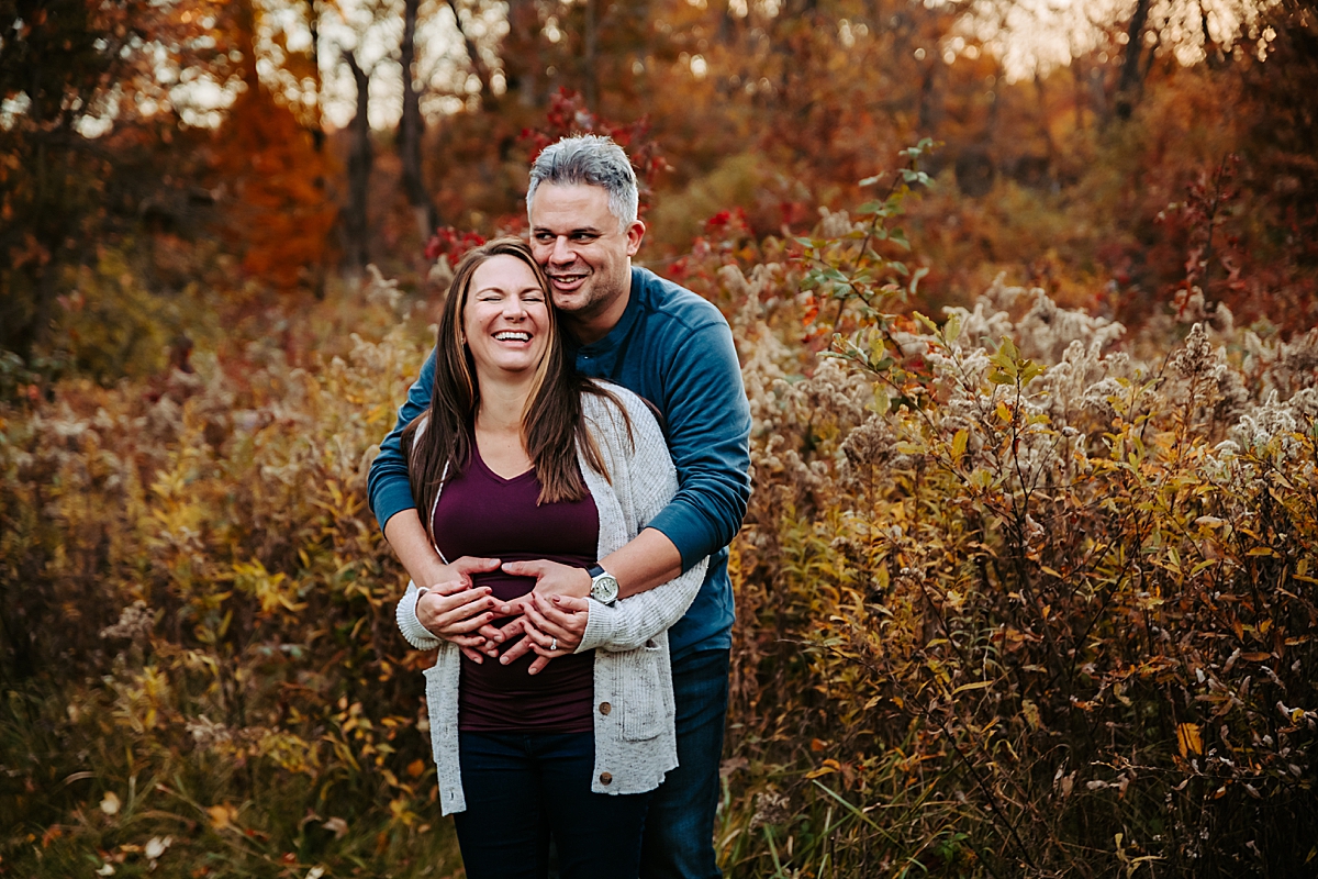 pregnant woman laughing with husband's arms wrapped around her smiling