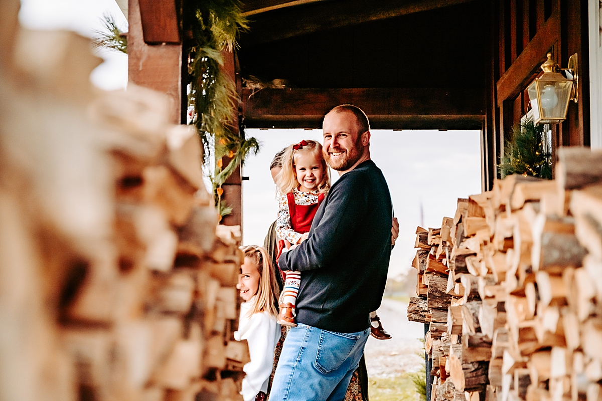 dad holding young daughter by wood pile