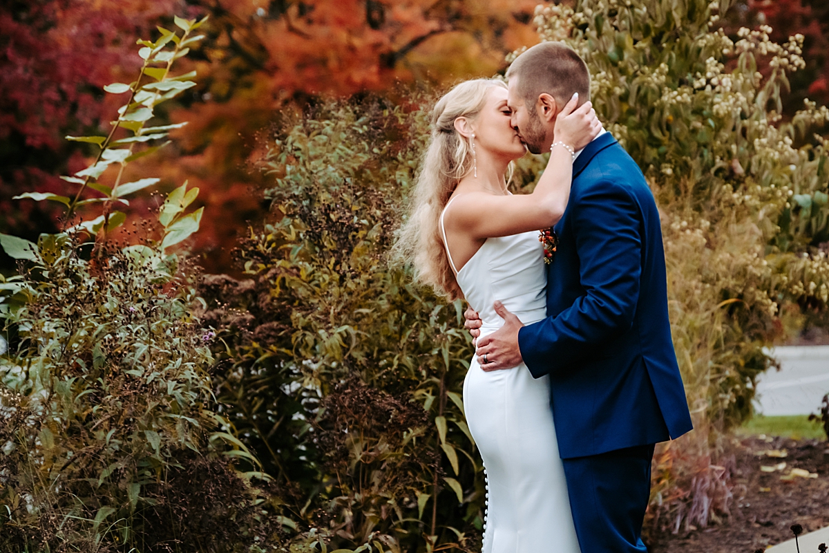 bride and groom kissing with fall trees in the background