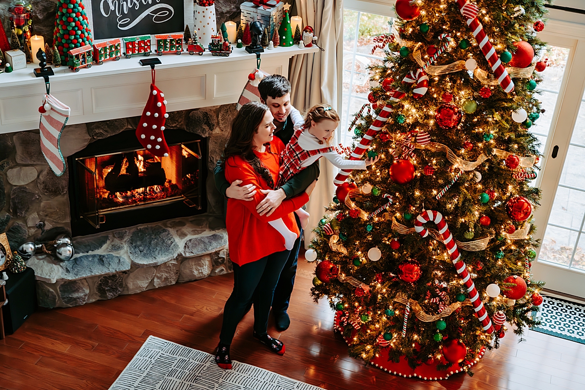 mom and dad holding young girl decorating large Christmas tree