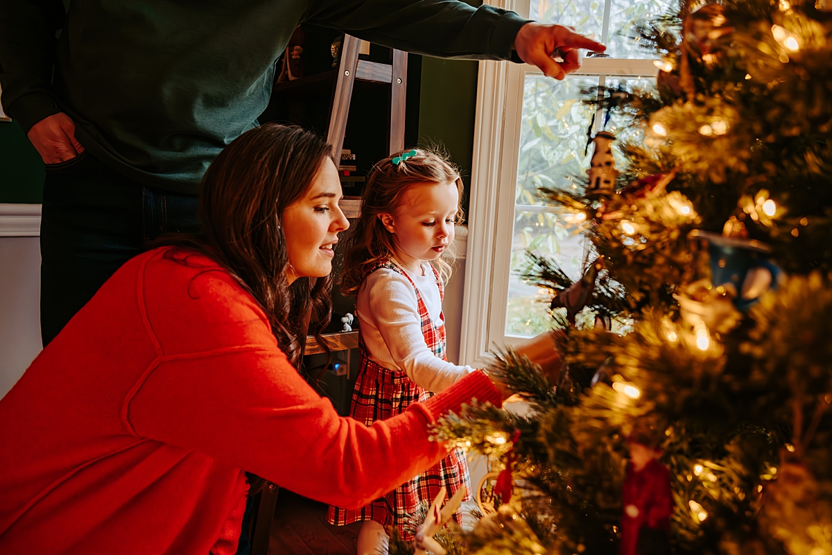 mom and dad helping young girl decorate Christmas tree