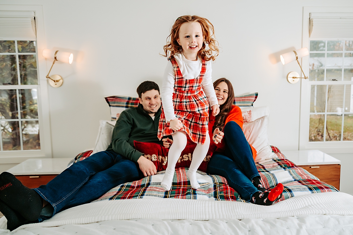 young girl jumping on bed with mom and dad smiling behind her