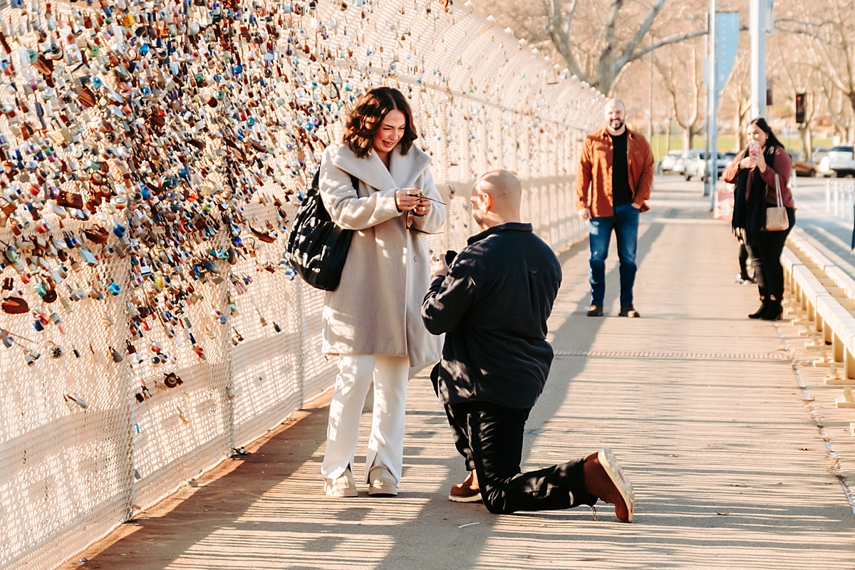 woman crying as man proposes down on one knee on Schenley Bridge in Pittsburgh PA
