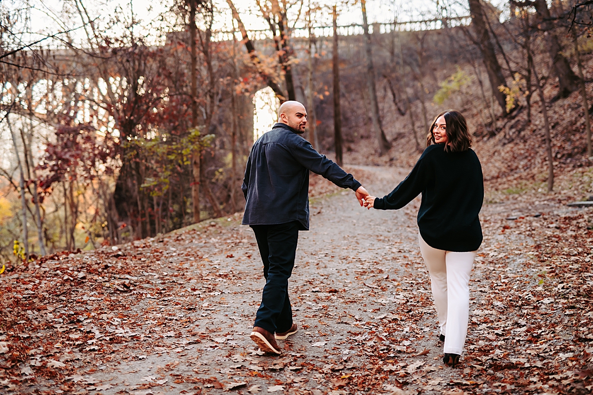 couple holding hands walking along path in Schenley Park