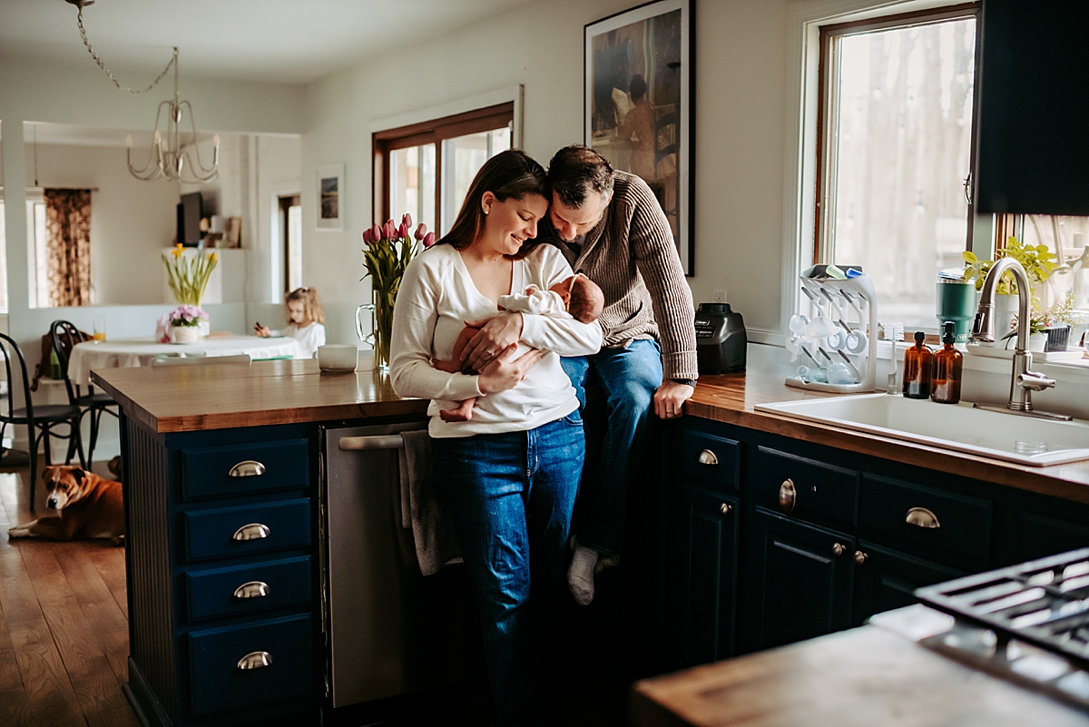 in home newborn session dad sitting on kitchen counter next to mom holding baby