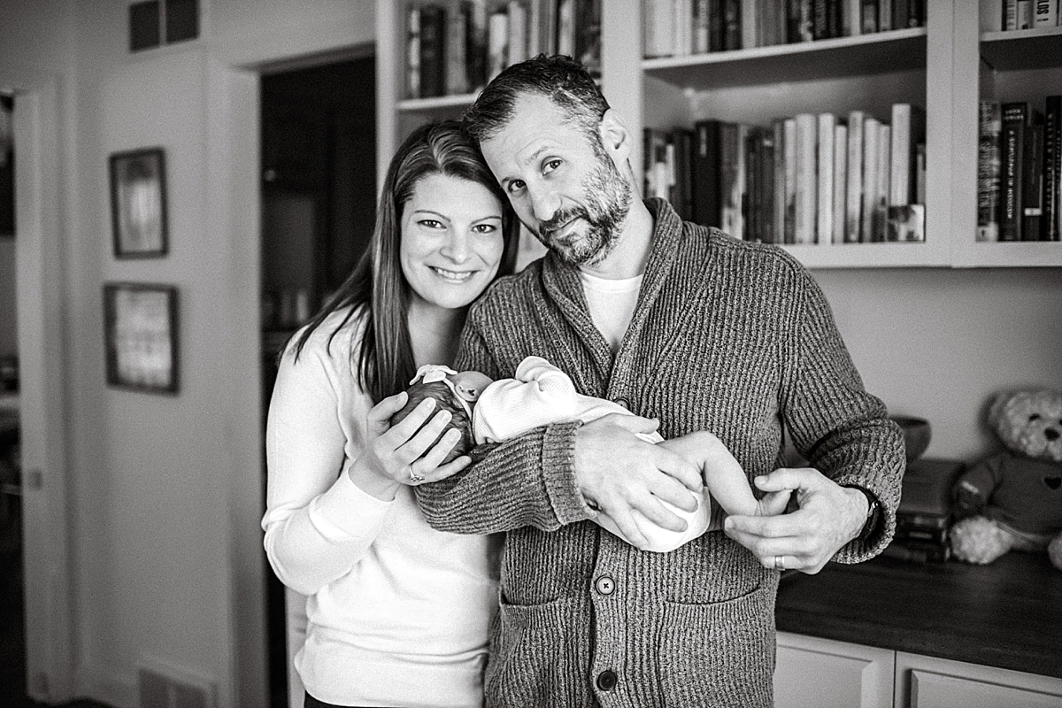 mom and dad holding newborn daughter in front of bookcase