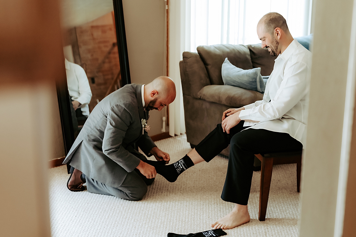 groomsman putting socks on groom sitting in chair