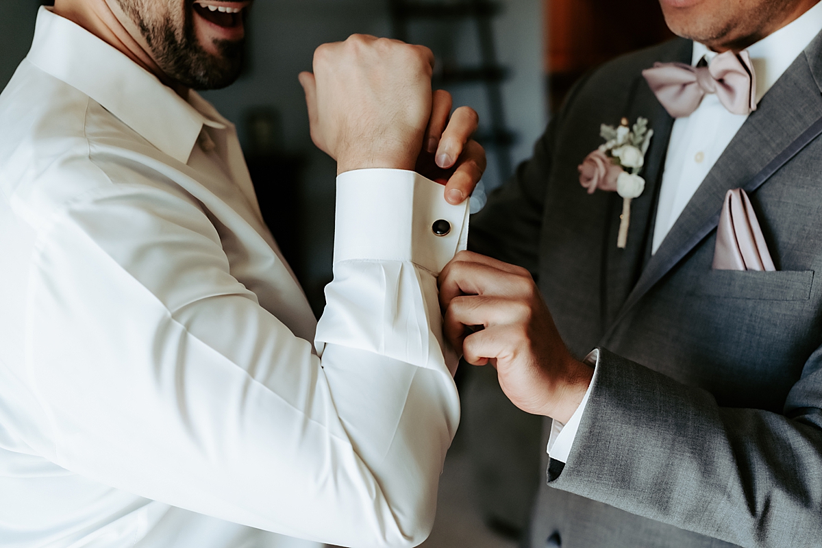 groomsman putting cuff links on groom's shirt