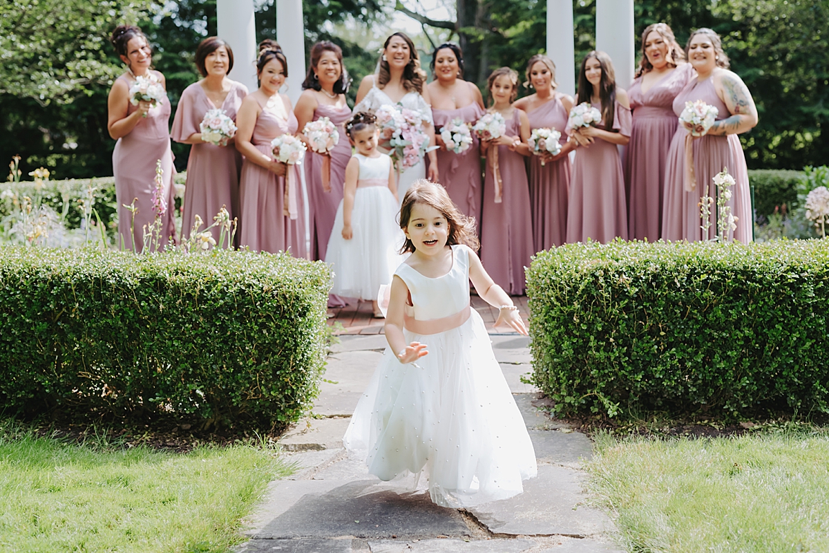 flower girl running with bridesmaids in dusty rose gowns laughing in the background