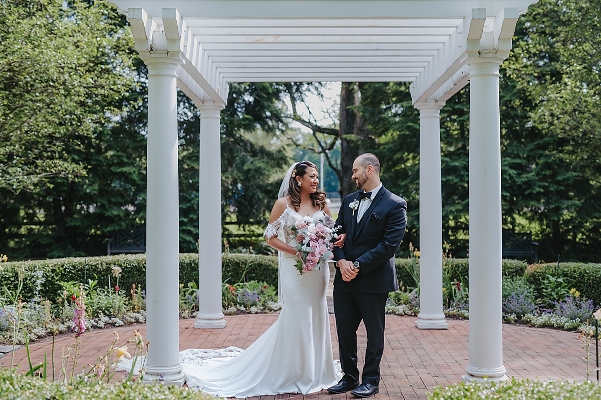 bride and groom standing under white arbor in garden 