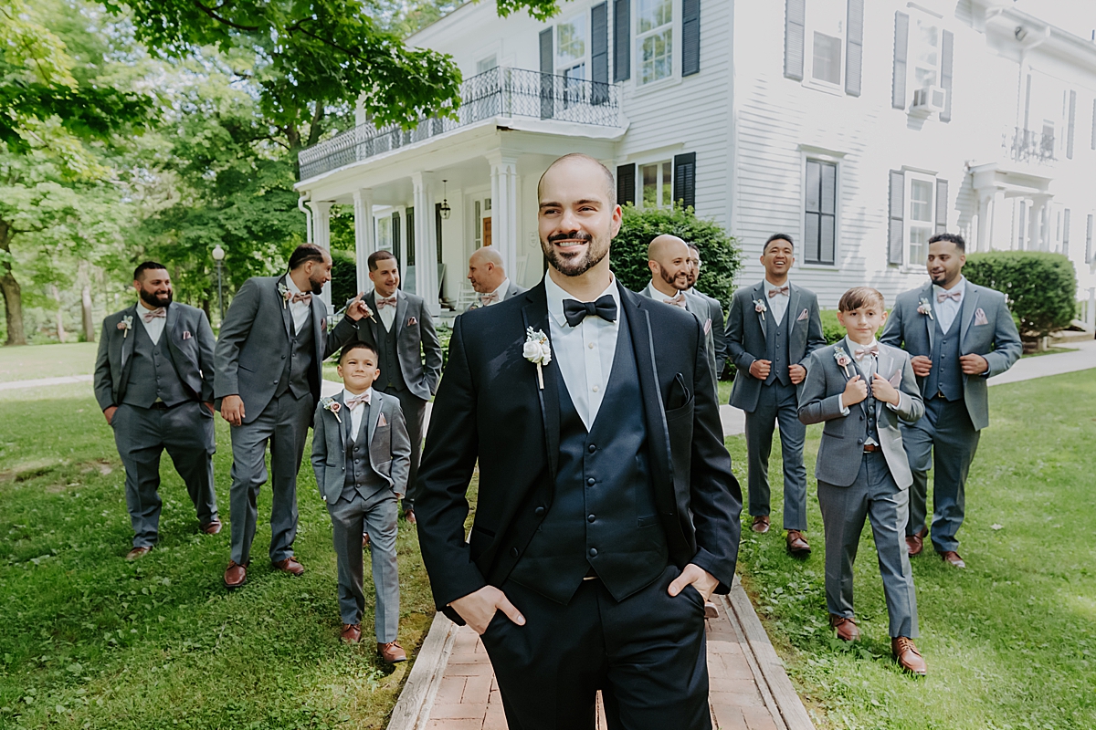 groom wearing black suit and bow tie walking with groomsmen in grey suits walking behind him