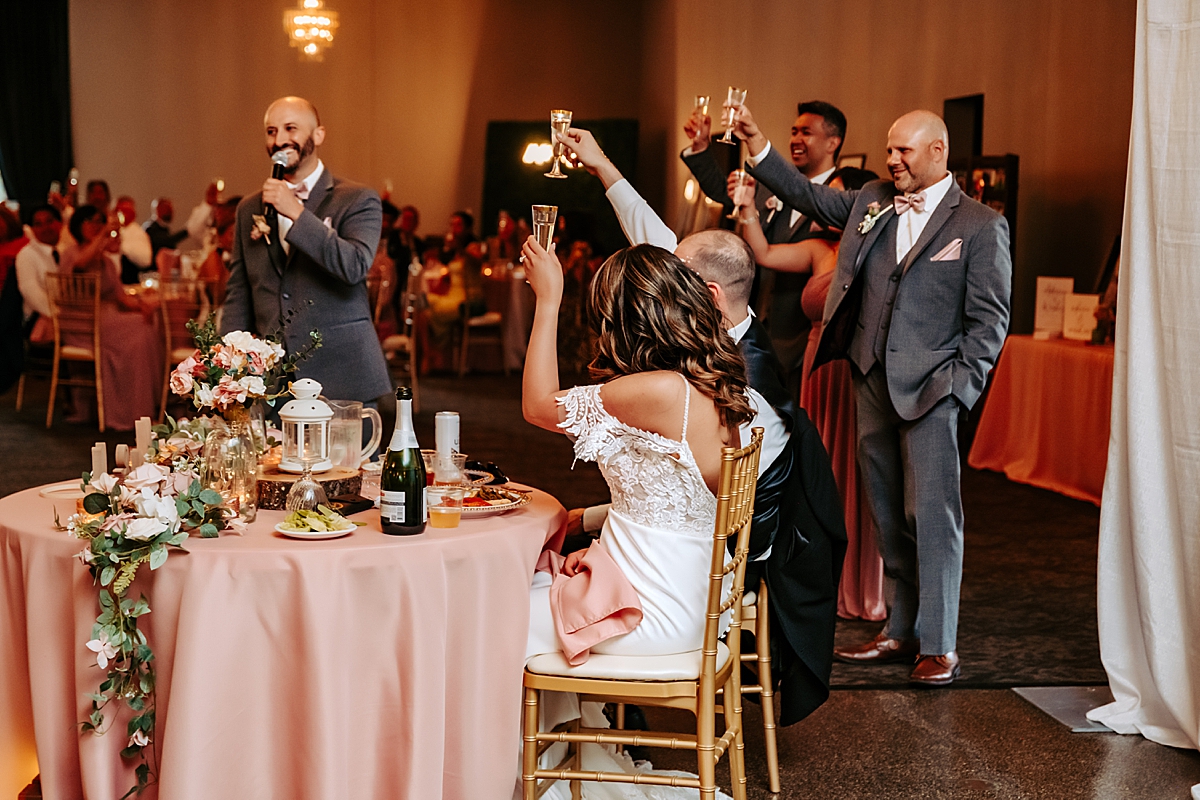 bride and groom sitting at head table toasting champagne classes