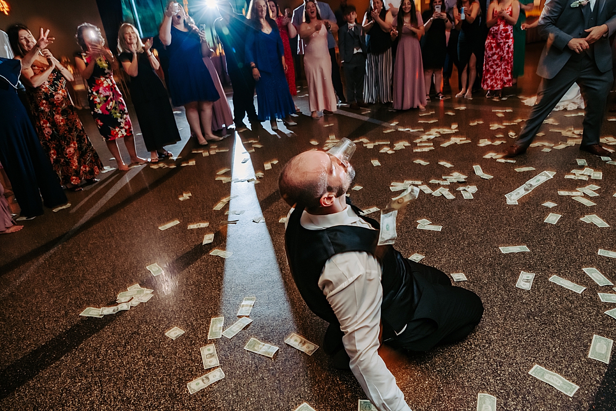 groom drinking alcohol while dancing with money on the ground all around him